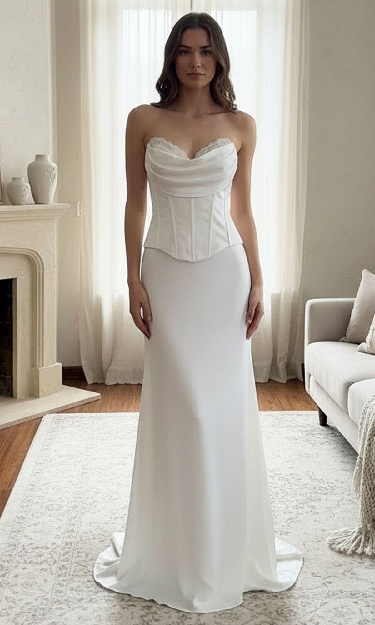A woman stands indoors wearing the Long Prom Dress: Amelia Couture 6137 in white, featuring a strapless satin design with a corset bodice and an elegant lace-up back.